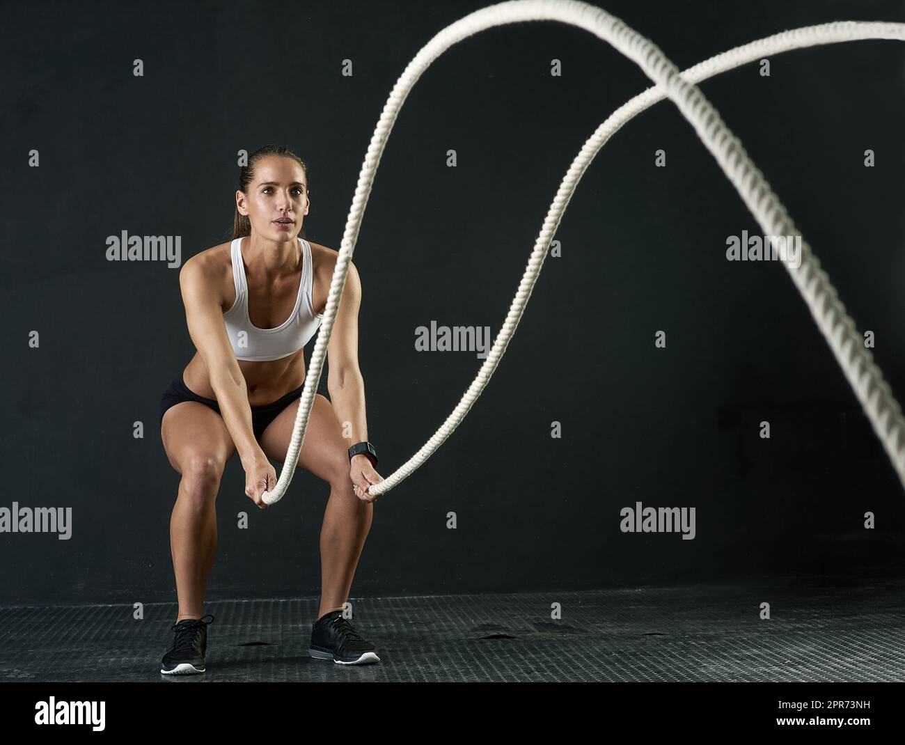 Preparatevi alla battaglia. Studio girato di una giovane donna attraente che si sta allenando con corde pesanti su uno sfondo scuro. Foto Stock