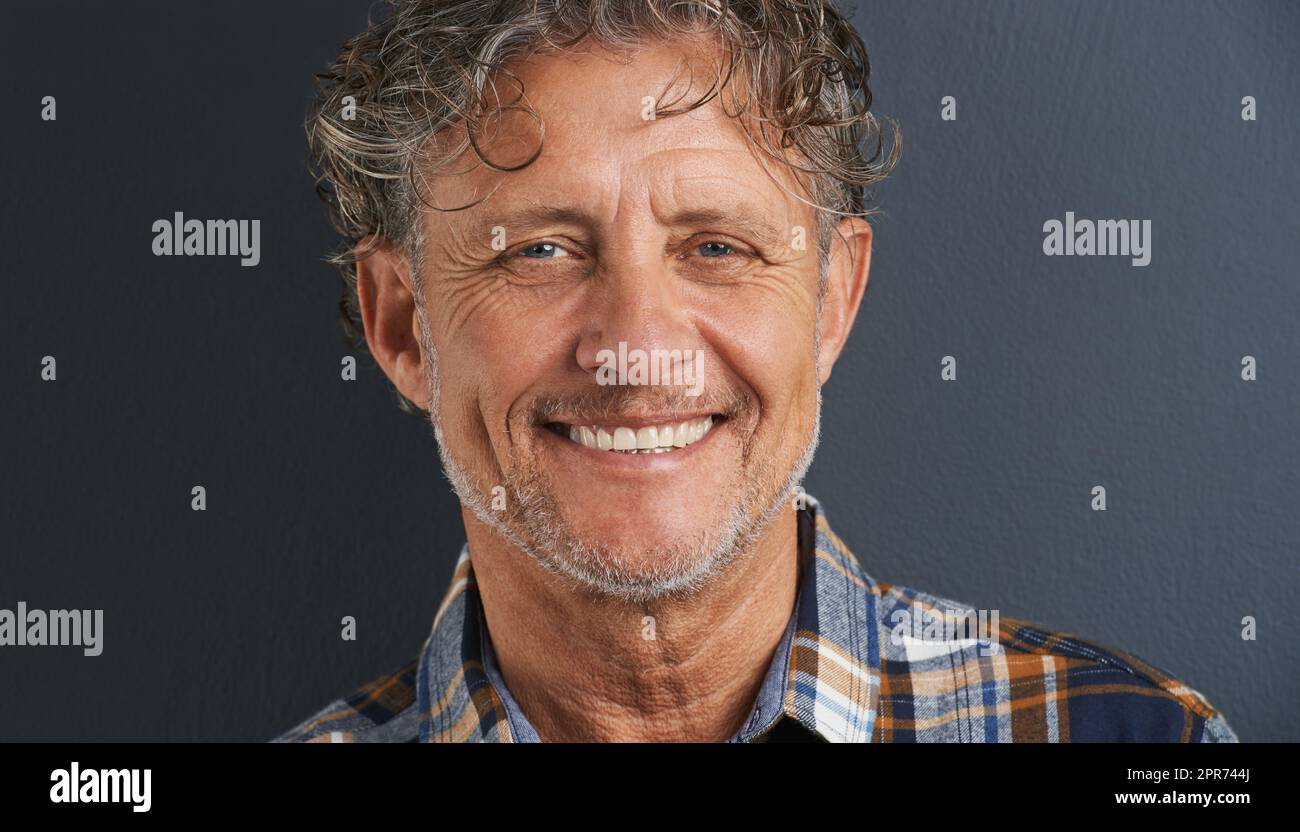 Un bel sorriso. Un ritratto corto di un uomo maturo felice in piedi su uno sfondo grigio. Foto Stock