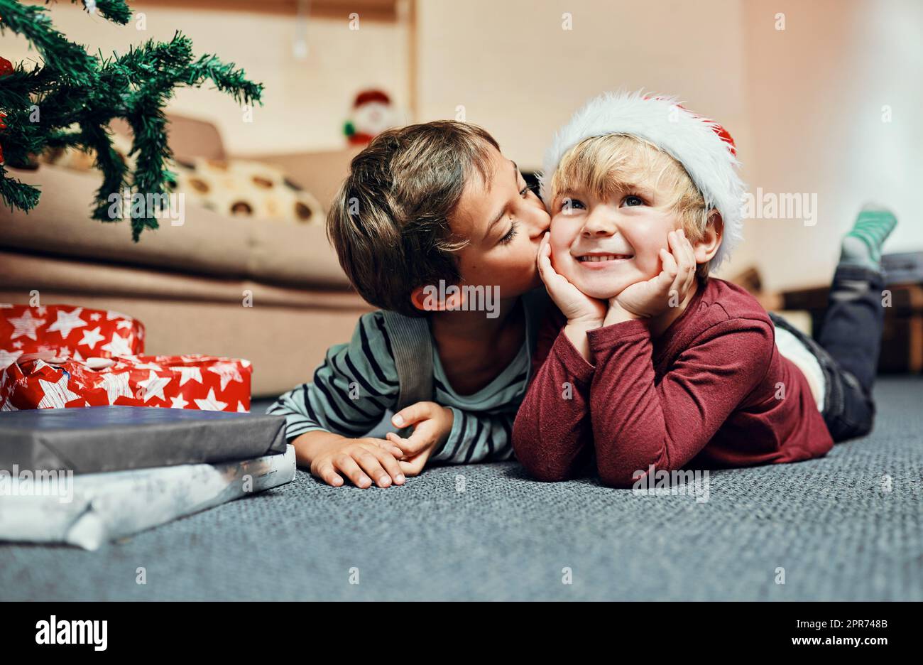 Santas regalo quest'anno non rivalità fratello. Scatto di un ragazzo adorabile che dà a suo fratello un bacio in attesa di aprire i loro regali di Natale. Foto Stock