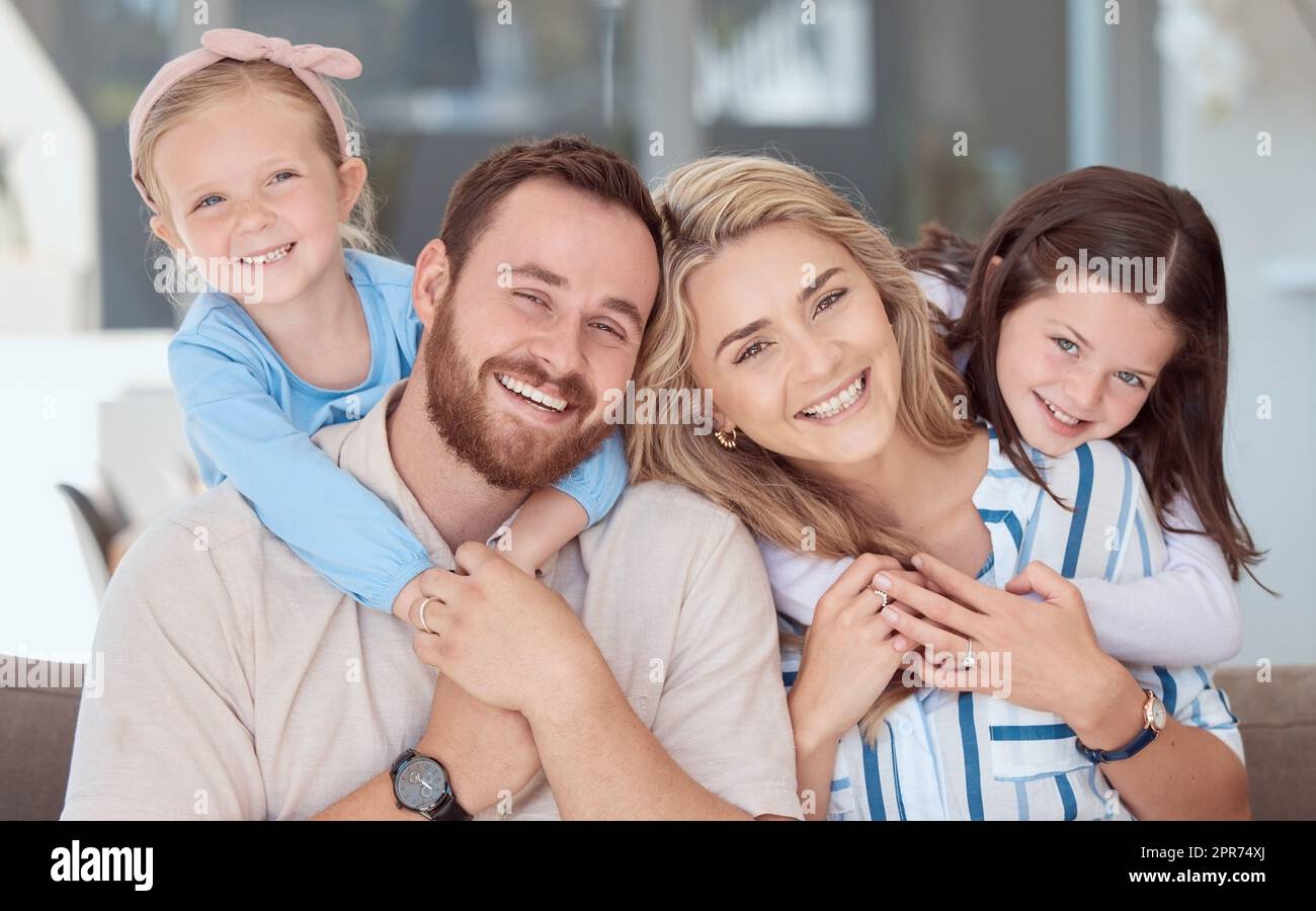 Felice famiglia caucasica di quattro persone sorridente mentre si rilassa su un divano insieme a casa. Genitori spensierati che legano con due figliole carine. Adorabili ragazze giocose che abbracciano mamma e papà Foto Stock