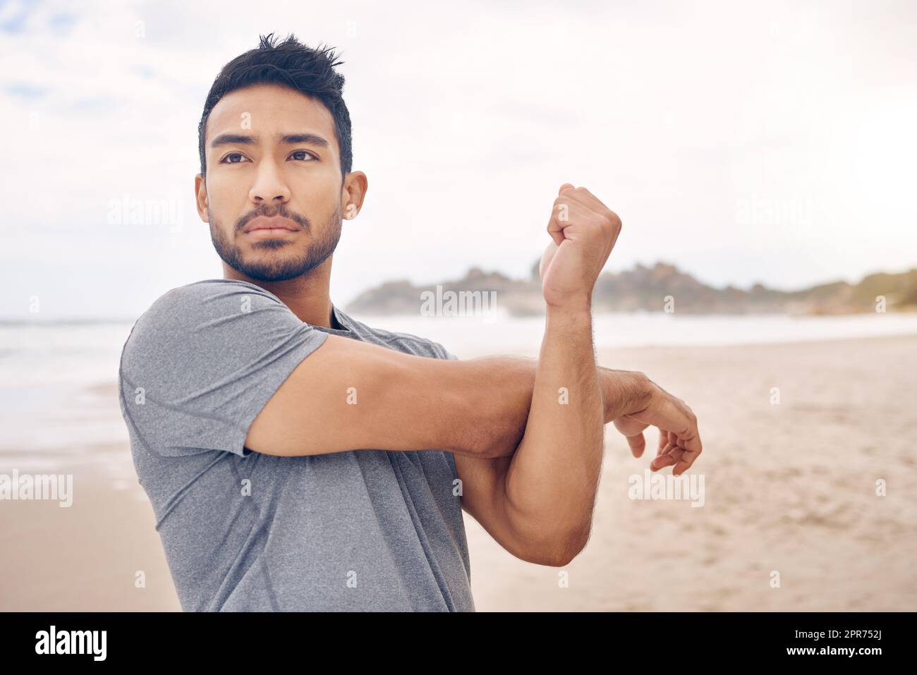 Sperimentando una messa a fuoco mentale e un impegno migliorati. Scatto di un giovane sportivo che allunga le braccia mentre si esercita sulla spiaggia. Foto Stock