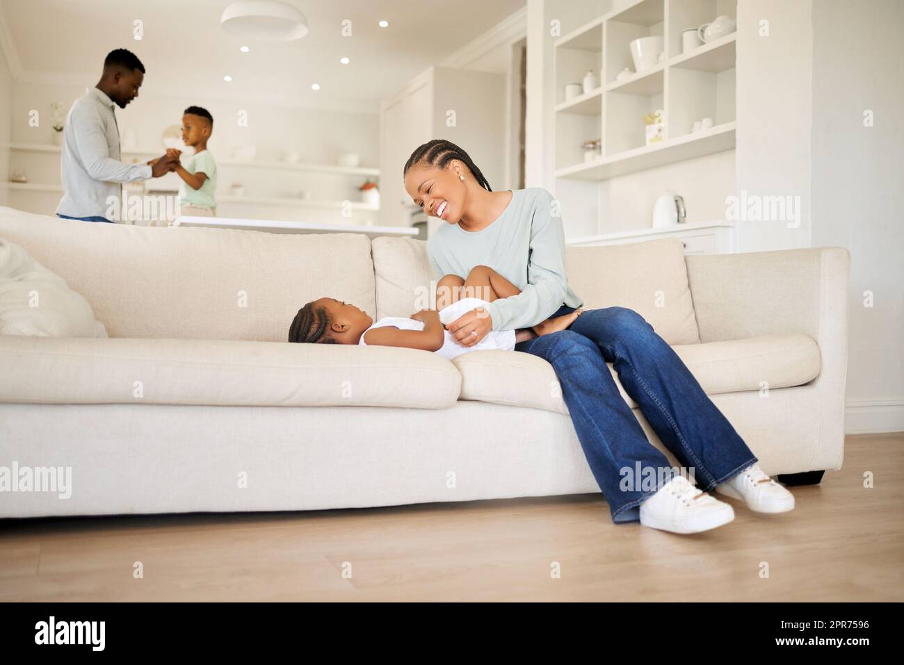 Giovane, allegra e felice madre afroamericana che gioca e si lega con sua figlia sul divano nel salotto di casa. Donna nera che gioca con la sua bambina carina nel weekend Foto Stock