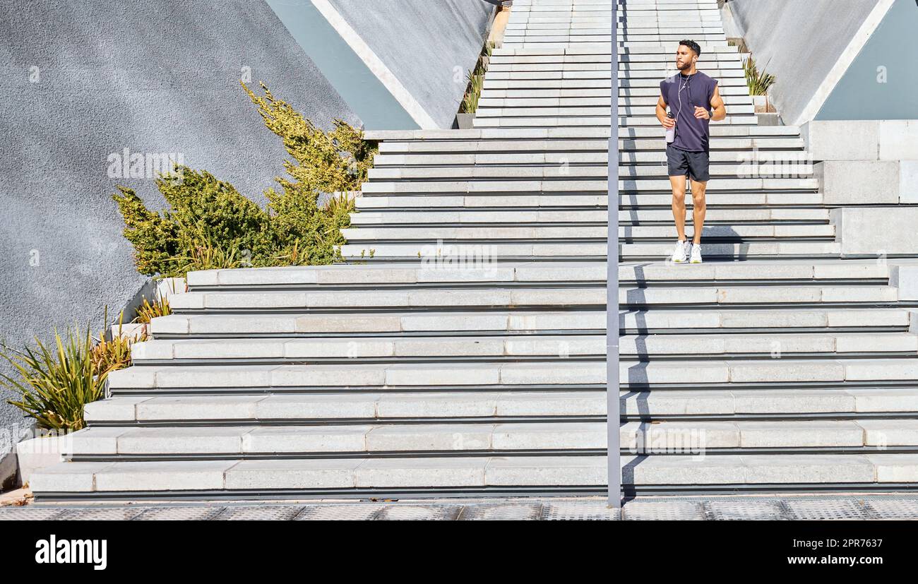 Tutto ciò di cui ho bisogno è me e una certa motivazione. Scatto di un giovane sportivo che ascolta musica e porta con sé una bottiglia d'acqua mentre si esercita all'aperto. Foto Stock