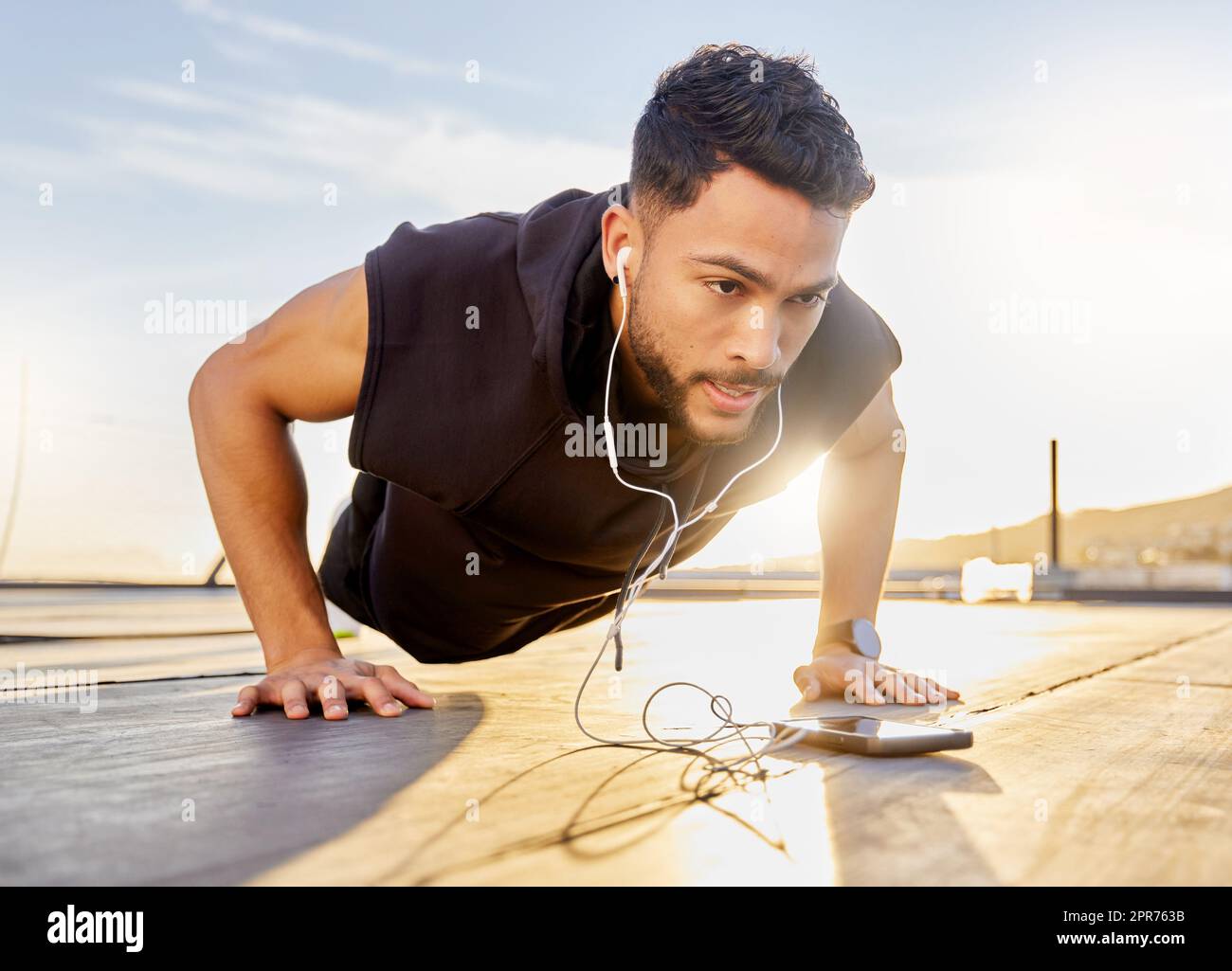 Spingi se vuoi raggiungere i tuoi obiettivi. Scatto di un giovane sportivo che indossa le cuffie mentre fai i push-up, su un tetto. Foto Stock