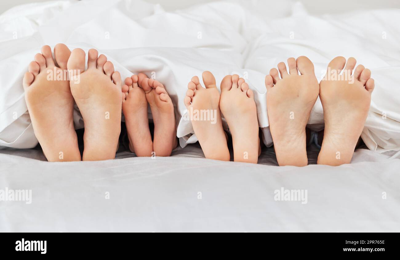 Otto piedi che riposano nell'amore. Scatto di una famiglia che si stendendo a piedi nudi su un letto a casa. Foto Stock