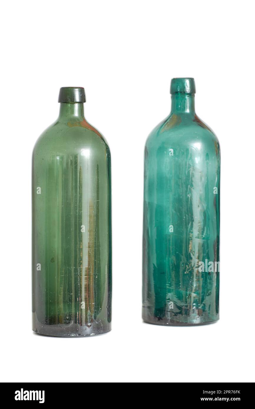 Due vecchie bottiglie di vetro vuote isolate su uno sfondo bianco dello studio con spazio per il copyspace. Vetreria antica colorata utilizzata come opera d'arte decorativa. Contenitori vintage trasparenti da riciclare o riutilizzare Foto Stock