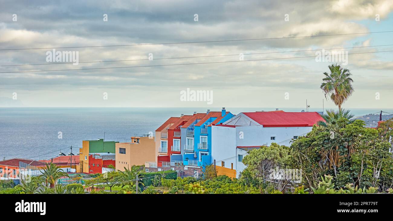 Vista panoramica di case dai colori vivaci, mare e cielo blu con nuvole e spazio copia a Santa Cruz de la Palma in Spagna. Palme tropicali che crescono da edifici infrustrutturati in destinazione turistica Foto Stock