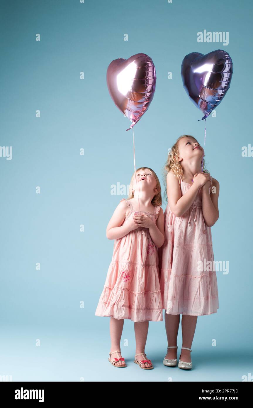 Abbiamo tanto divertimento insieme. Scatto di due sorelle carine che giocano con palloncini a cuore contro uno sfondo studio. Foto Stock