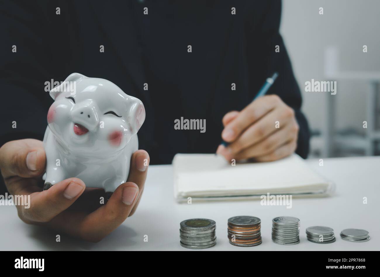 Uomo d'affari persona Hand Holding risparmio moneta piggybank soldi sul tavolo.Business Finance conto investimento imposta economia assicurazione e piano pensione concetto. Foto Stock