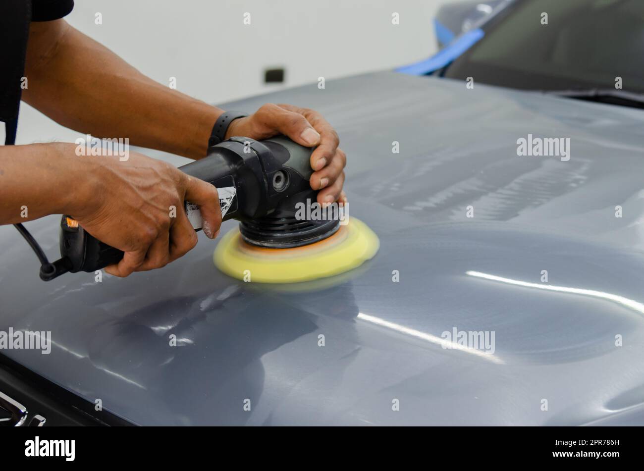 Uomo che tiene attrezzo lucidare meccanico auto riparazione dettaglio cofano auto graffio manutenzione in garage carwash lavoro. Foto Stock
