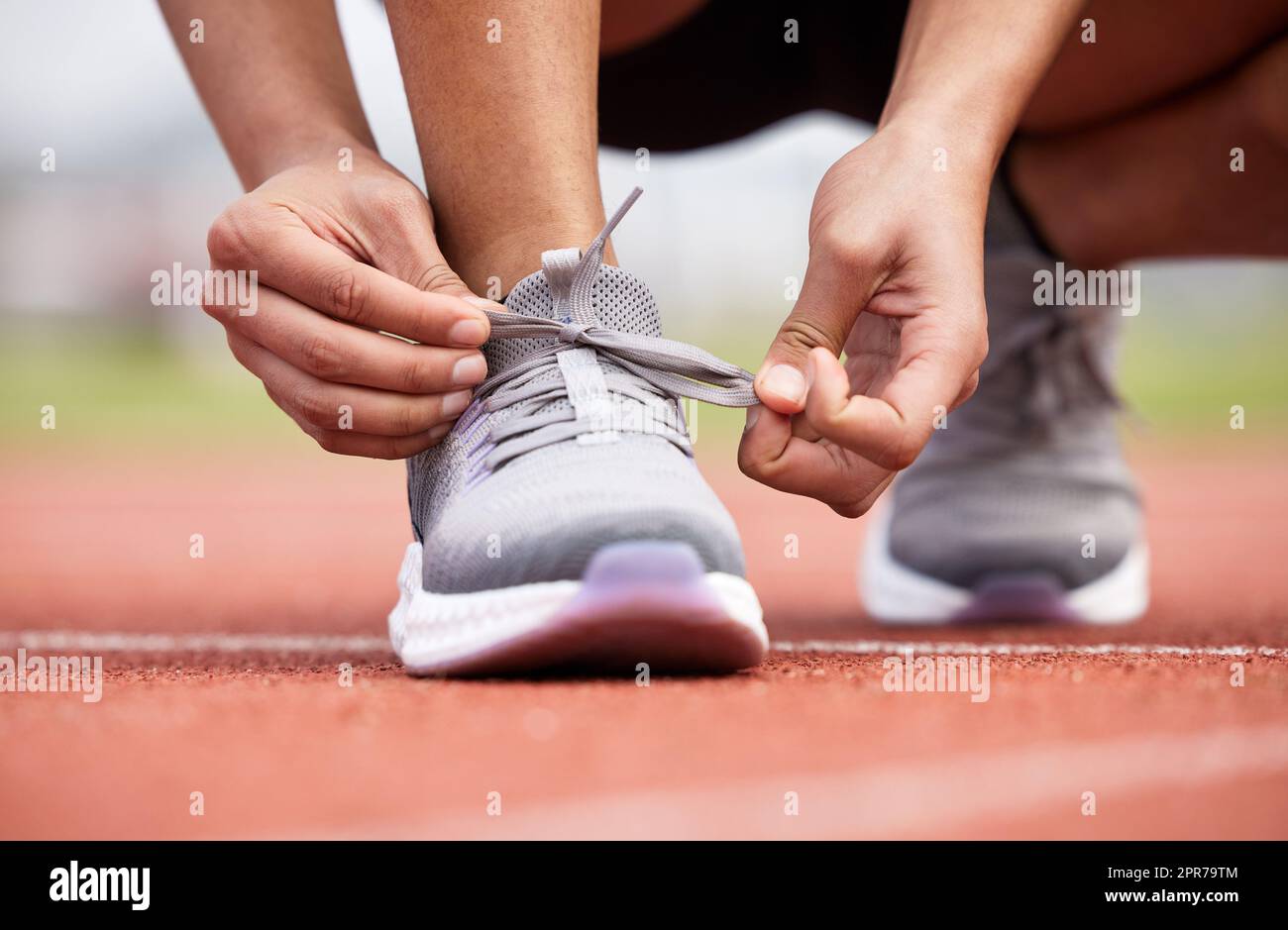 Non può permettersi qualsiasi scivolamento aumenta. Un atleta femminile irriconoscibile che lega i suoi lacci fuori sulla pista. Foto Stock