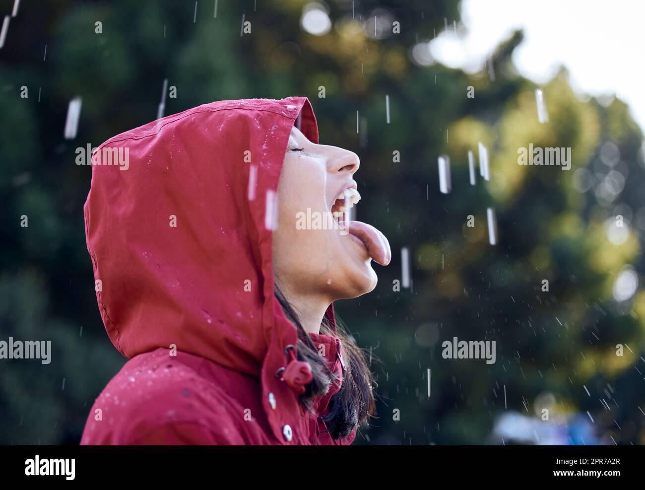 Mi sento di nuovo come un bambino, la pioggia lo fa. Una giovane donna che attacca la sua lingua per sentire la pioggia fuori. Foto Stock