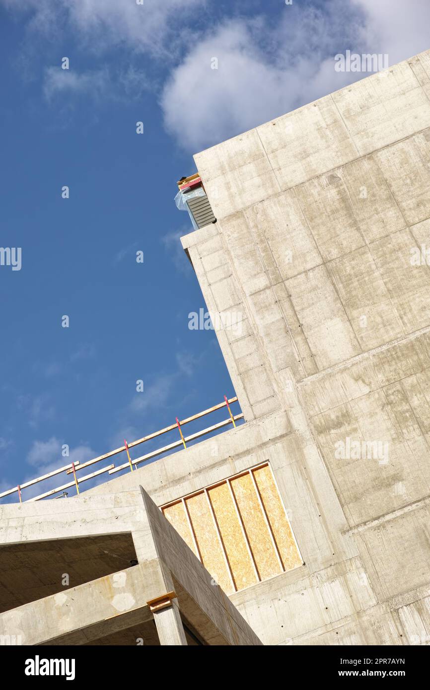 Esterno di un edificio in cemento contro un cielo blu nuvoloso. Vista dettagliata di un alto edificio residenziale o di uffici realizzato con lastre di cemento esposte. Fase di costruzione della ristrutturazione e aggiunta della casa Foto Stock