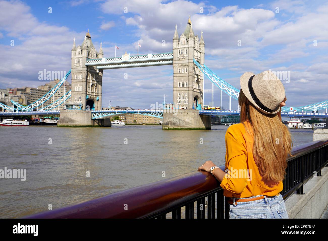 Ragazza turistica appoggiata sulla ringhiera sul lungofiume del Tamigi con il famoso punto di riferimento di Tower Bridge a Londra, Regno Unito Foto Stock
