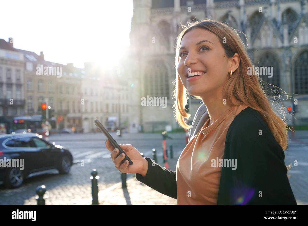 Ritratto di giovane donna sul lato della strada in attesa di un taxi in possesso di uno smartphone. Chiamare un taxi con un concetto di app per telefono. Foto Stock