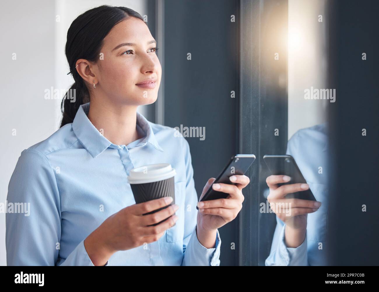 Donna d'affari seria che pensa, guardando la vista dalla finestra mentre beve un caffè, si connette a un'app online. Un professionista che si prende una pausa, scrivendo sul suo smartphone Foto Stock