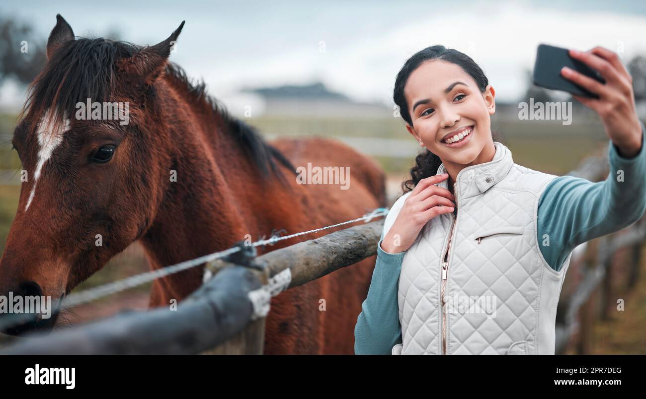 Voglio che tutti vedano la sua bellezza: Una donna attraente che prende un selfie mentre si posa con un cavallo in un pascolo chiuso in una fattoria. Foto Stock