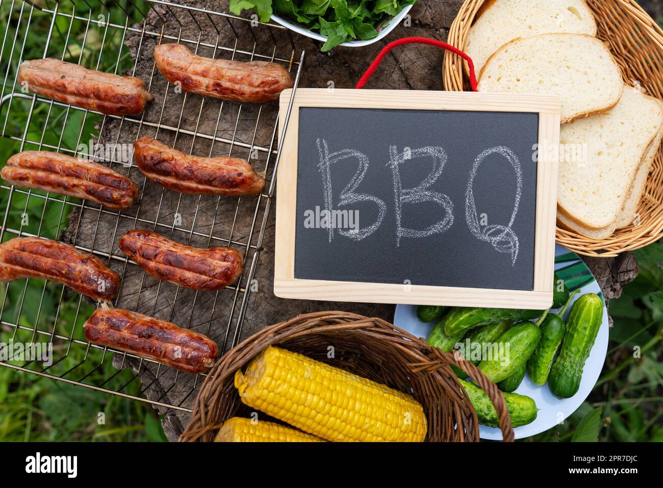 Iscrizione barbecue sulla lavagna, salsicce alla griglia, mais, pane. Attività ricreative all'aperto. Foto Stock