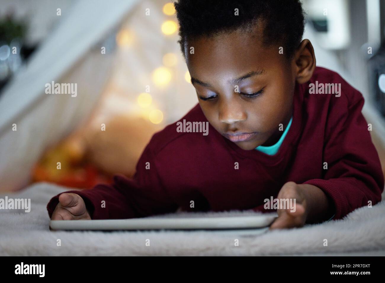 È troppo tardi, un adorabile ragazzino che usa un tablet digitale durante la notte a casa. Foto Stock