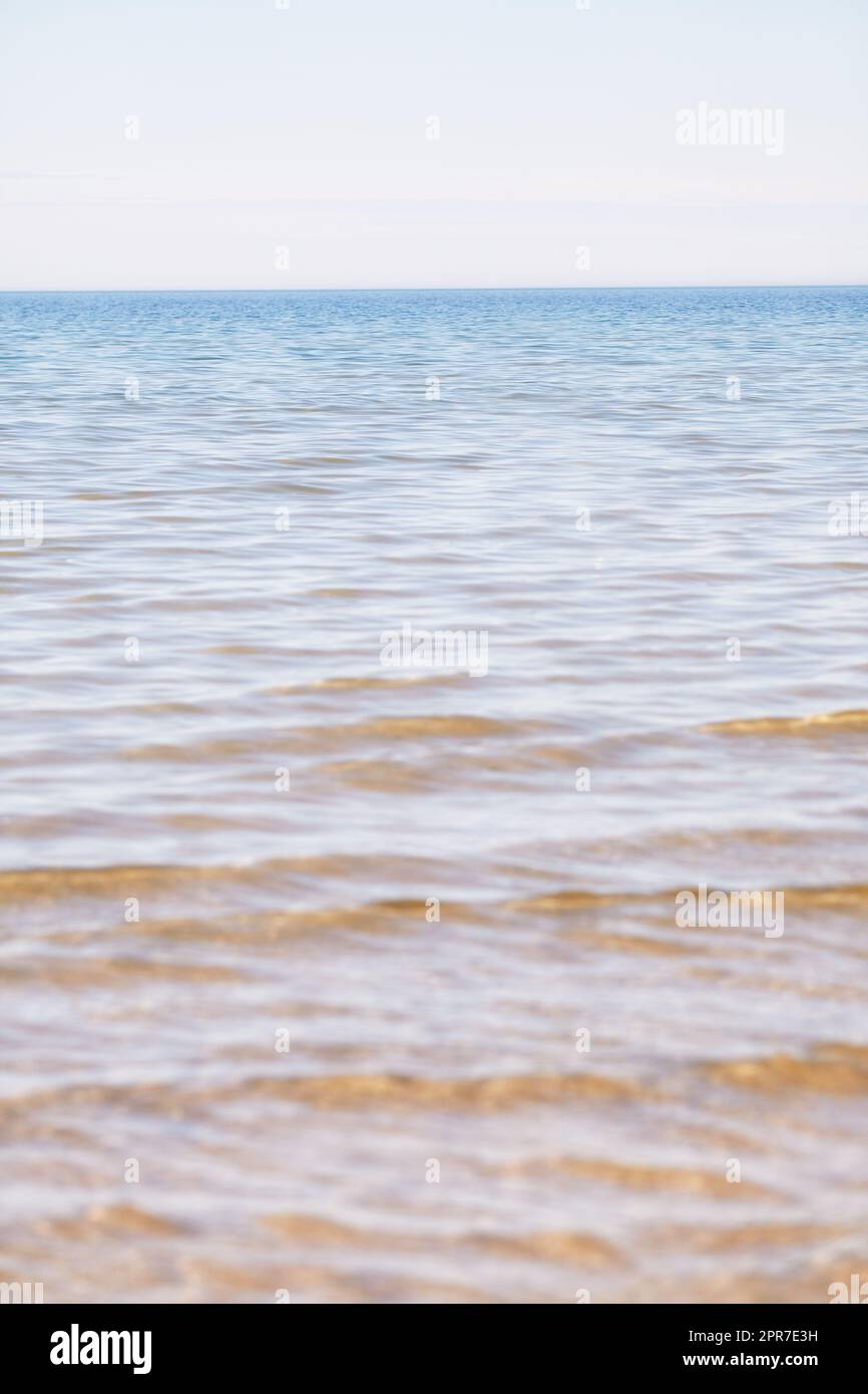 Copia lo spazio sul mare con un cielo azzurro sullo sfondo sopra l'orizzonte. Calme acque oceaniche in una spiaggia vuota. Tranquillo e panoramico paesaggio costiero per una rilassante vacanza estiva zen nella natura Foto Stock