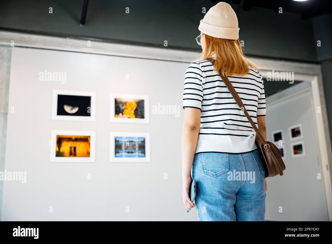 Donna asiatica che guarda una galleria d'arte di fronte a quadri colorati incorniciati Foto Stock