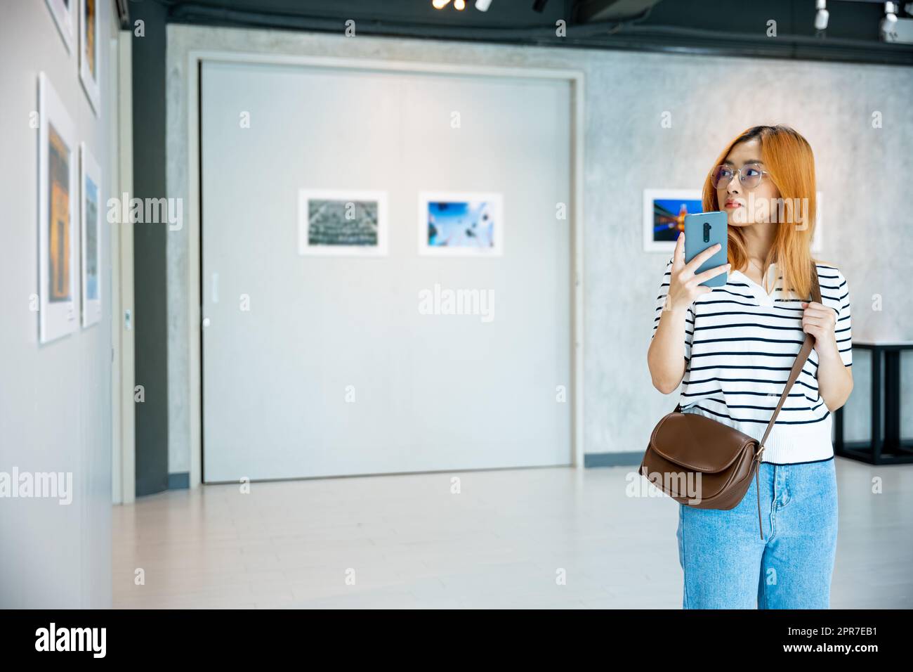 La donna visitatrice in piedi scatta foto della galleria d'arte davanti a quadri incorniciati Foto Stock