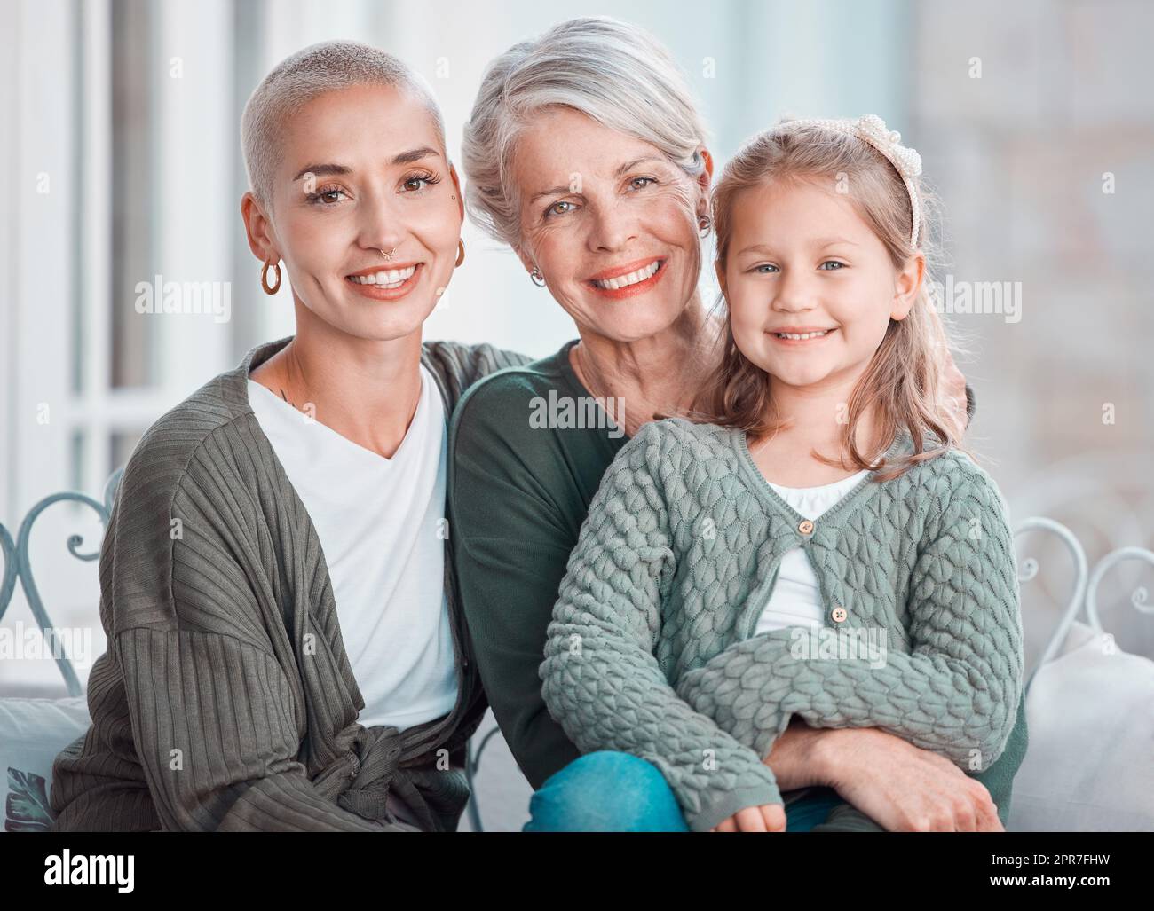 Ritratto di tre generazioni di femmine che guardano e sorridono alla fotocamera. Adorabile bambina che si lega con la madre e la nonna a casa Foto Stock