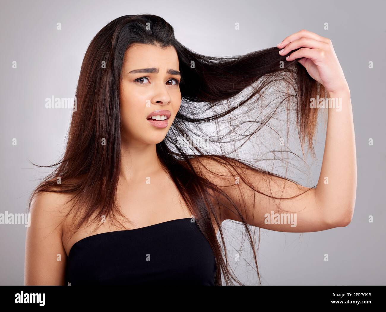 Perché è così annodato. Studio ritratto di una giovane donna attraente che ha un cattivo giorno capelli su uno sfondo grigio. Foto Stock