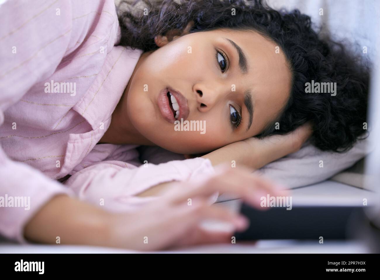 Im impostare la mia sveglia un po 'più tardi. Una giovane donna che controlla il suo telefono mentre si trova nel suo letto. Foto Stock