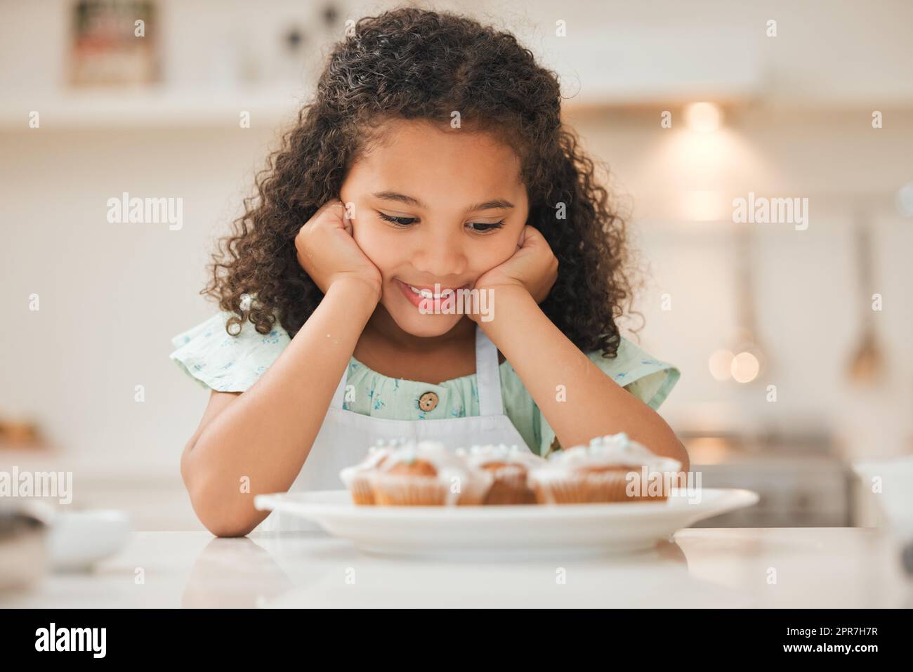 Non so se potessi aspettare più a lungo: Una bambina che aspetta pazientemente di mangiare i cupcake appena sfornati. Foto Stock