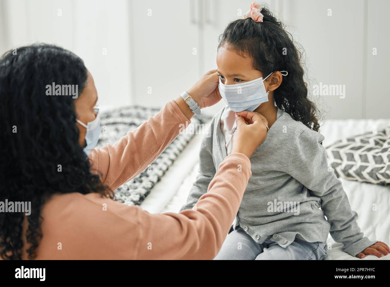 Non possiamo mai dimenticare le nostre maschere: Una giovane madre e una figlia che mettono le maschere a casa. Foto Stock