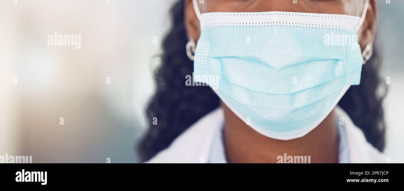 Closeup medico donna afroamericana che indossa una maschera mentre si trova in ospedale. Essere al sicuro durante la pandemia del virus della corona. Fermare la diffusione della covid 19. Salute e sicurezza in campo medico Foto Stock