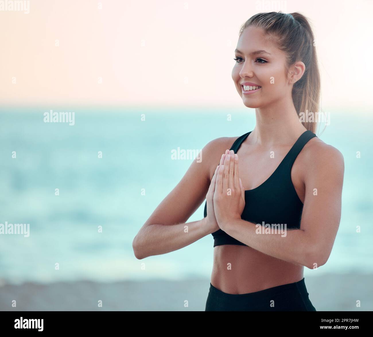 Bella donna che medita mentre pratica esercizi di yoga sulla spiaggia. Giovane atleta zen che si allena all'aperto. Trovare la pace interiore, l'equilibrio e diventare sani. Focalizzata sullo stile di vita del fitness Foto Stock