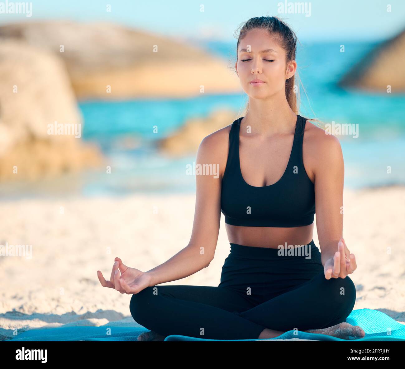 Bella donna che medita mentre pratica esercizi di yoga sulla spiaggia. Giovane atleta zen che si allena all'aperto. Trovare la pace interiore, l'equilibrio e diventare sani. Focalizzata sullo stile di vita del fitness Foto Stock