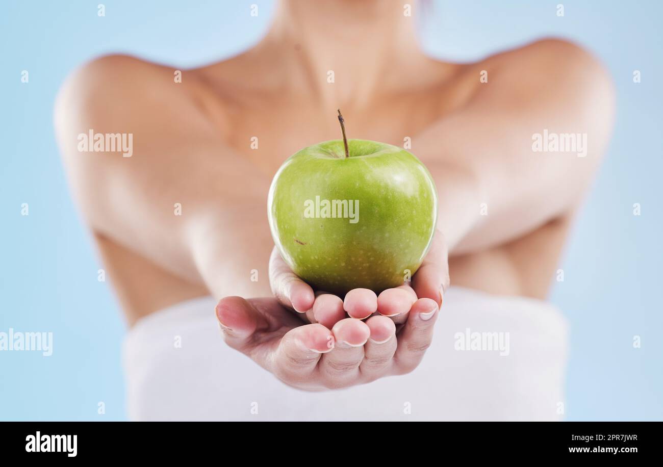 Bella giovane donna mista con una mela isolata in studio su uno sfondo blu. Il suo regime di cura della pelle la mantiene fresca. Per la pelle luminosa, mangiare sano. Ricco di vitamine e nutrienti Foto Stock