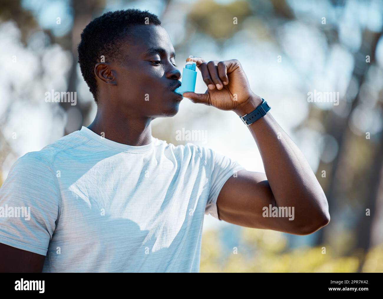 Un giovane africano che si prende una pausa da un allenamento per usare la sua pompa per l'asma. Allenate l'atleta usando il suo inalatore per l'asma durante un attacco d'asma mentre vi allenate all'aperto. Uomo atletico che utilizza un trattamento medico Foto Stock
