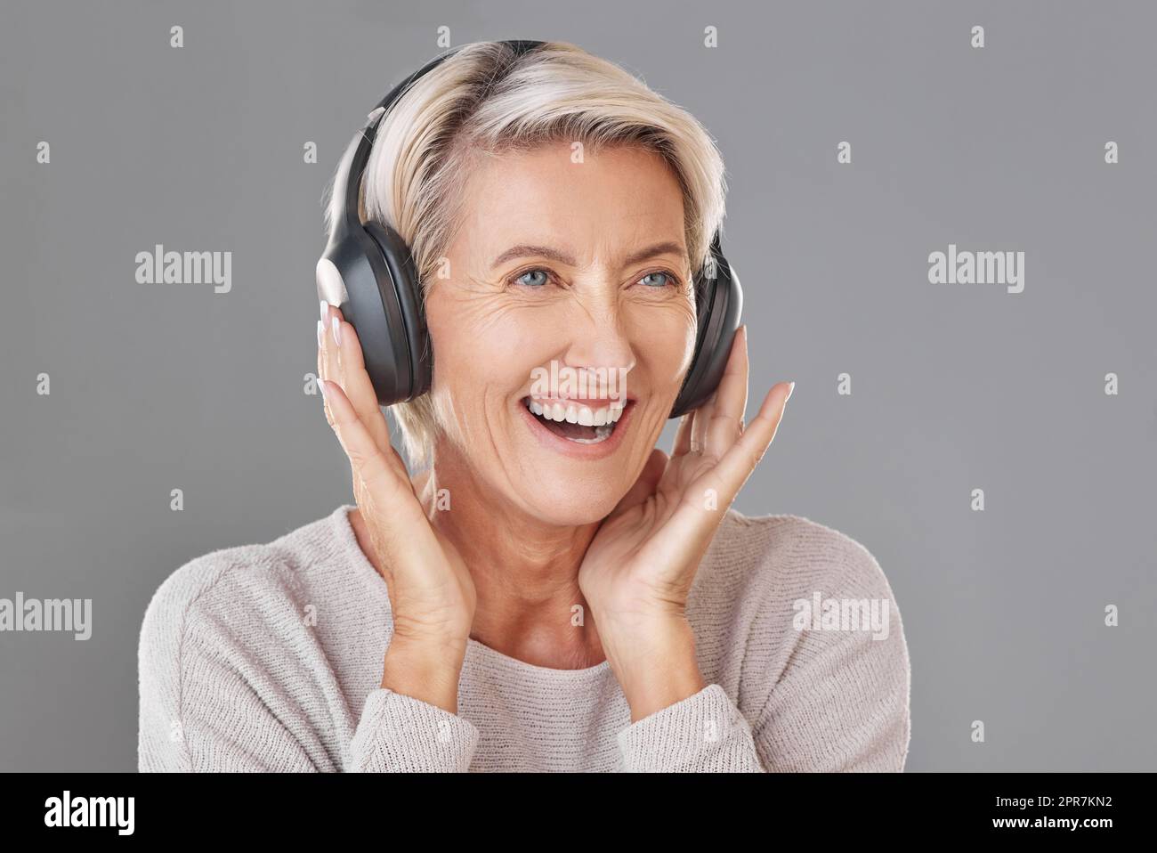 Una donna matura felice isolata in uno studio di registrazione e che indossa cuffie per ascoltare musica. Sorridente anziano caucasico con i capelli grigi che si gode la musica ad alto volume. Giovane e giocoso Foto Stock