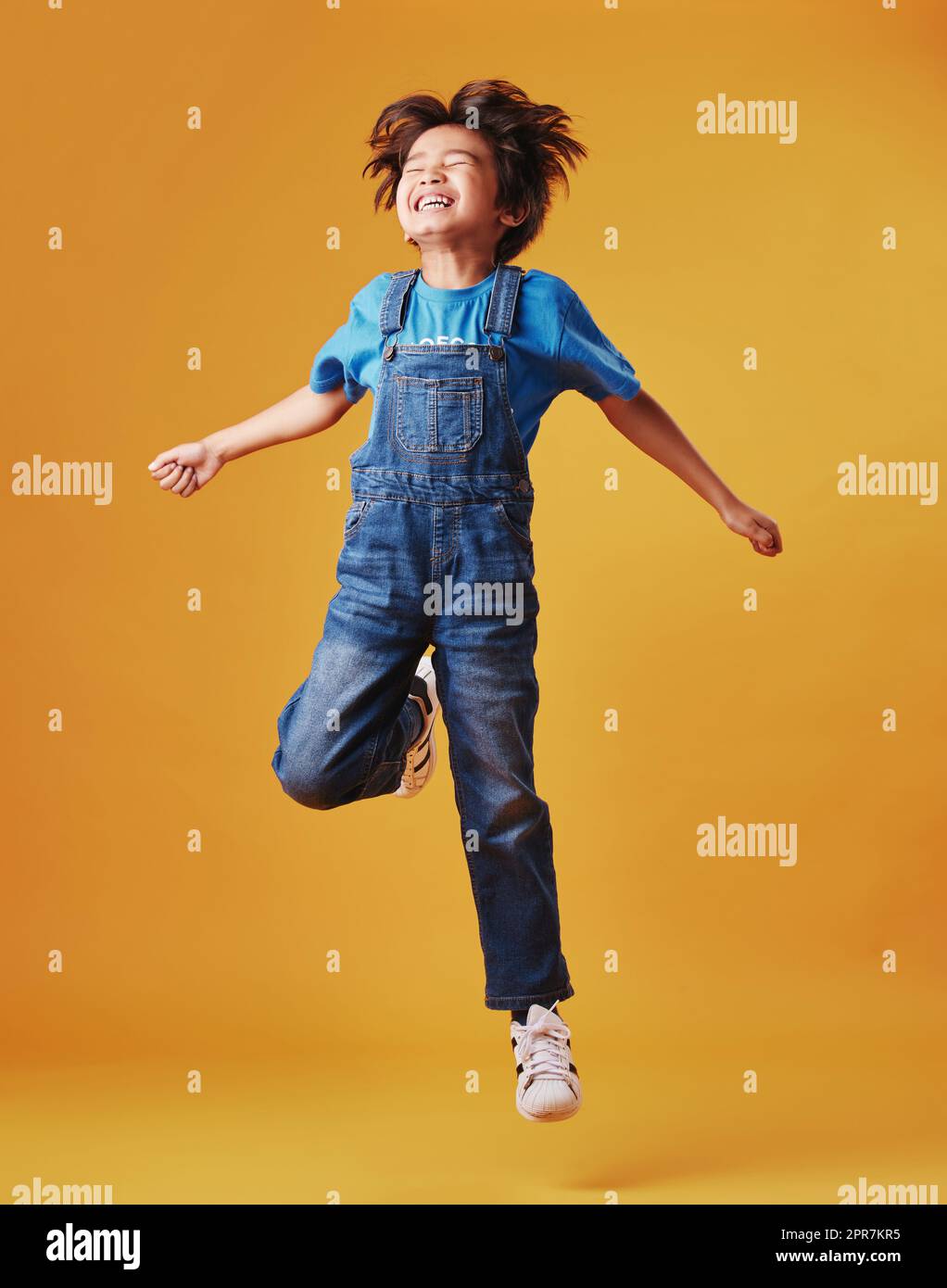 Un bambino simpatico misto che indossa abiti casual mentre si diverte ed è energico contro uno sfondo arancione copyspace. Il bambino asiatico è attivo Foto Stock