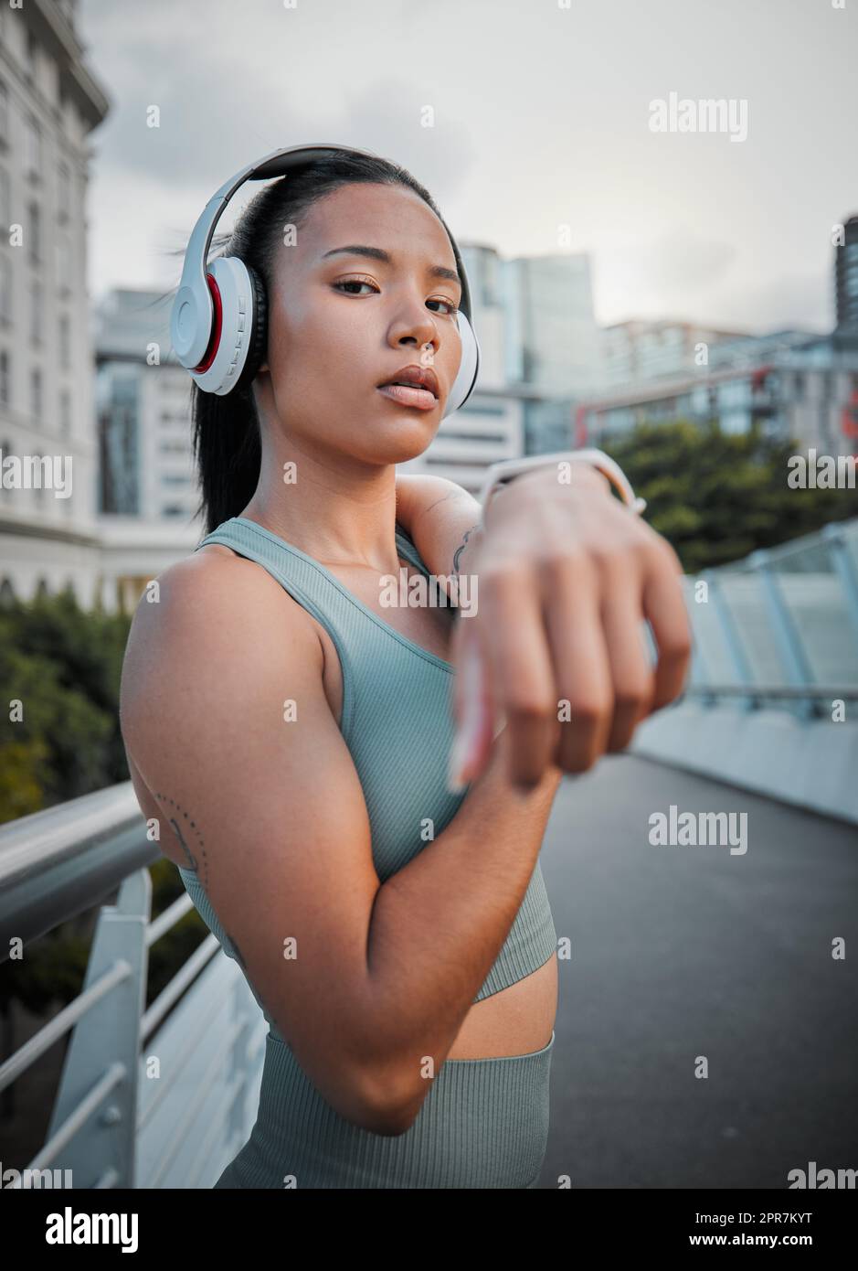 Giovane atleta femminile che indossa cuffie e ascolta musica mentre allunga i muscoli prima di una corsa all'aperto in città. Riscaldarsi prima di fare esercizio fisico per migliorare la sua salute e il suo stile di vita Foto Stock