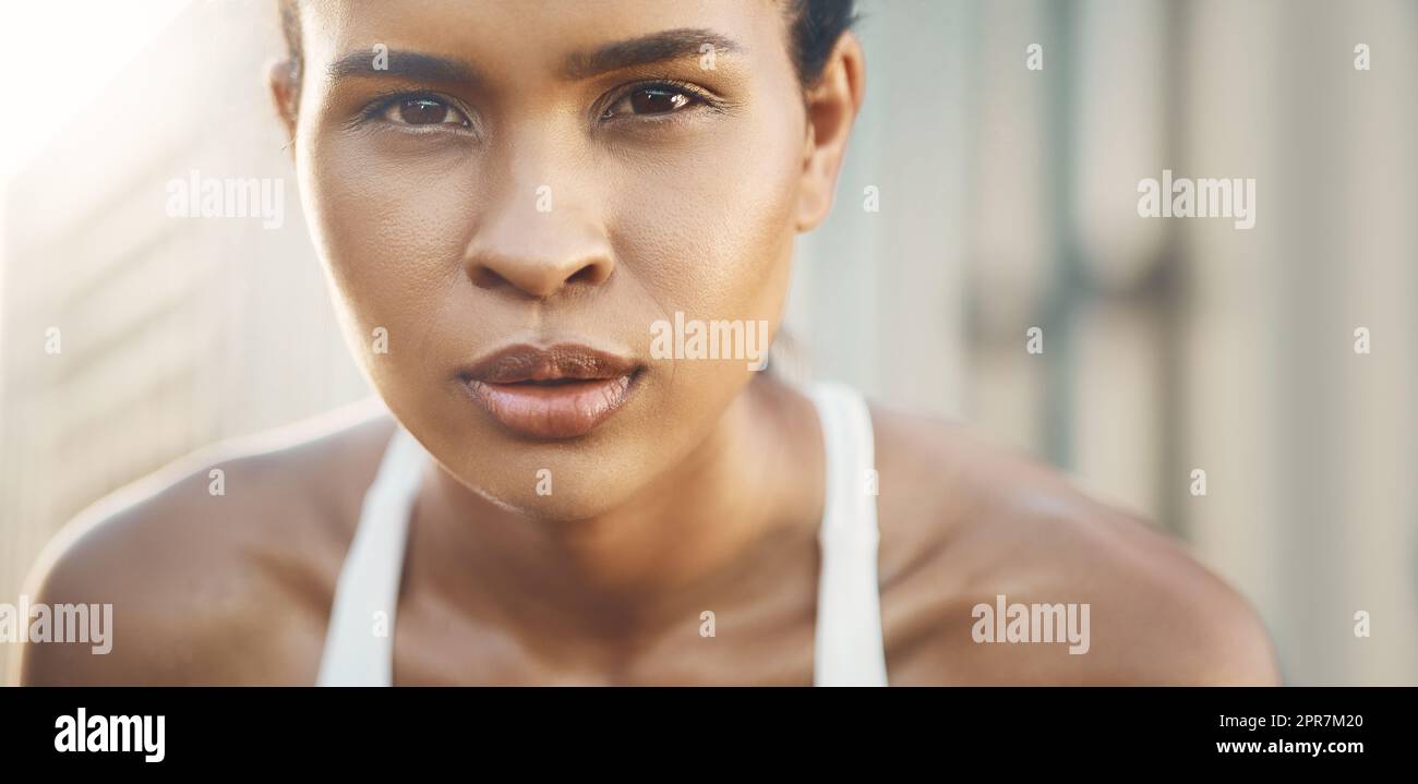 Ritratto in primo piano di una giovane donna ispanica che si riposa per riprendere fiato dopo una corsa o una corsa in un ambiente urbano all'aperto. Atleta femminile che sembra stanca ma determinata dopo un intenso esercizio cardiovascolare Foto Stock