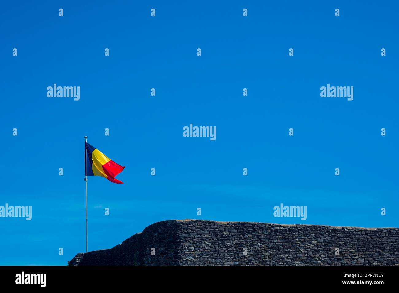 Bandiera belga che sventola su un muro medievale contro un cielo blu Foto Stock