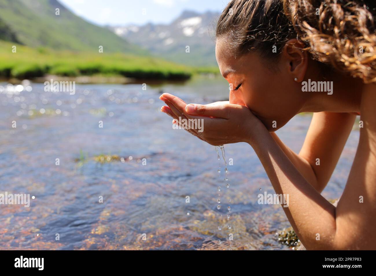 Donna che beve acqua non trattata dal fiume Foto Stock