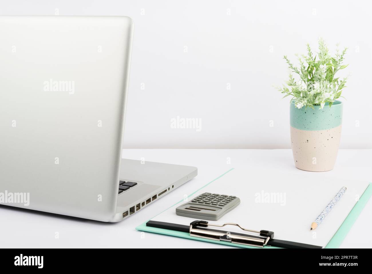 Lap Top, Appunti vuoti con carta, matita, Calcolatrice e vaso in ufficio. Scrivania con computer, notebook vuoto e Flower. Cancelleria sul posto di lavoro. Foto Stock