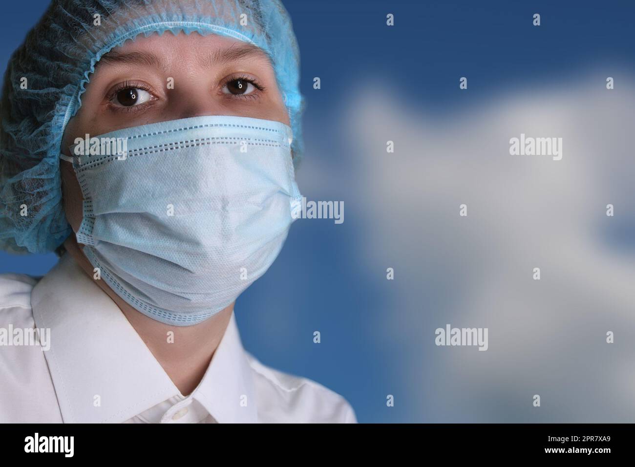 Ritratto ravvicinato di una donna medico in un berretto medico e maschera contro il cielo blu. Foto Stock