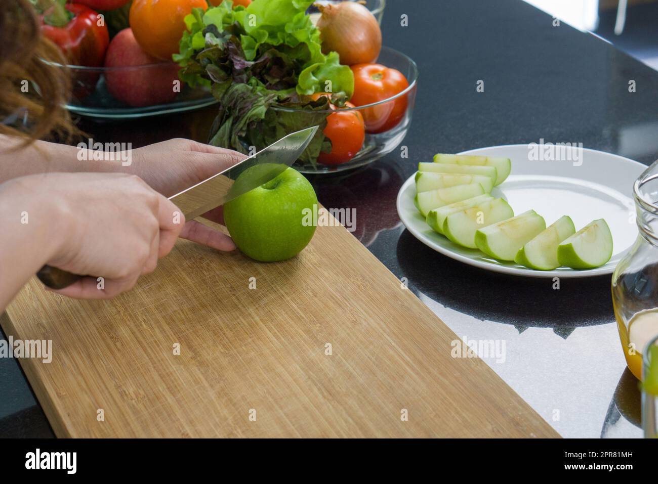 https://c8.alamy.com/compit/2pr81mh/chiudi-la-mano-tenendo-il-coltello-che-taglia-la-mela-verde-su-un-tagliere-di-legno-la-frutta-a-fette-viene-posta-su-un-piatto-una-ciotola-di-vetro-con-una-varieta-di-frutta-e-verdura-e-posizionata-sul-bancone-della-cucina-2pr81mh.jpg