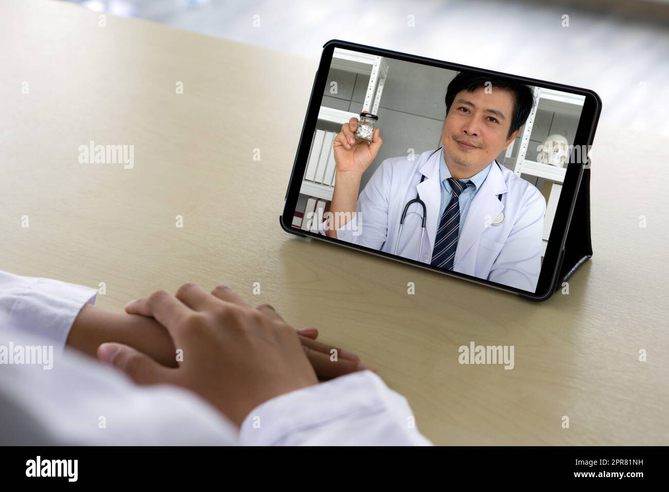 Vista posteriore del farmacista in abito bianco sedersi alla scrivania avere conferenza webcam su tablet computer con il medico asiatico circa capsula medica. Concetto di sanità e medicina. Foto Stock