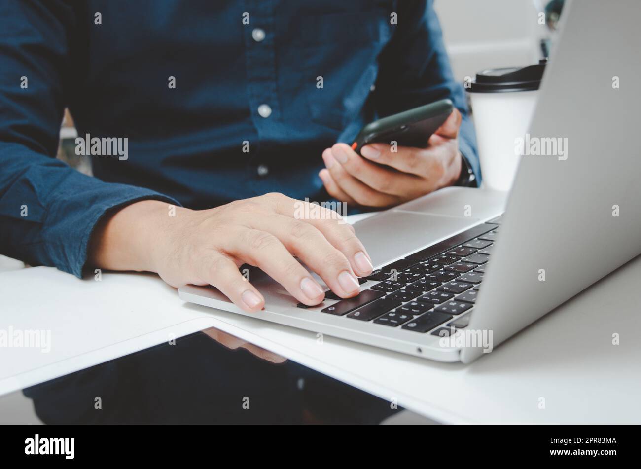 Uomo d'affari che tiene in mano smartphone mobile marketing digitale tecnologia online e comunicazione social network con computer portatile navigazione in Internet e shopping online on desk concept. Foto Stock