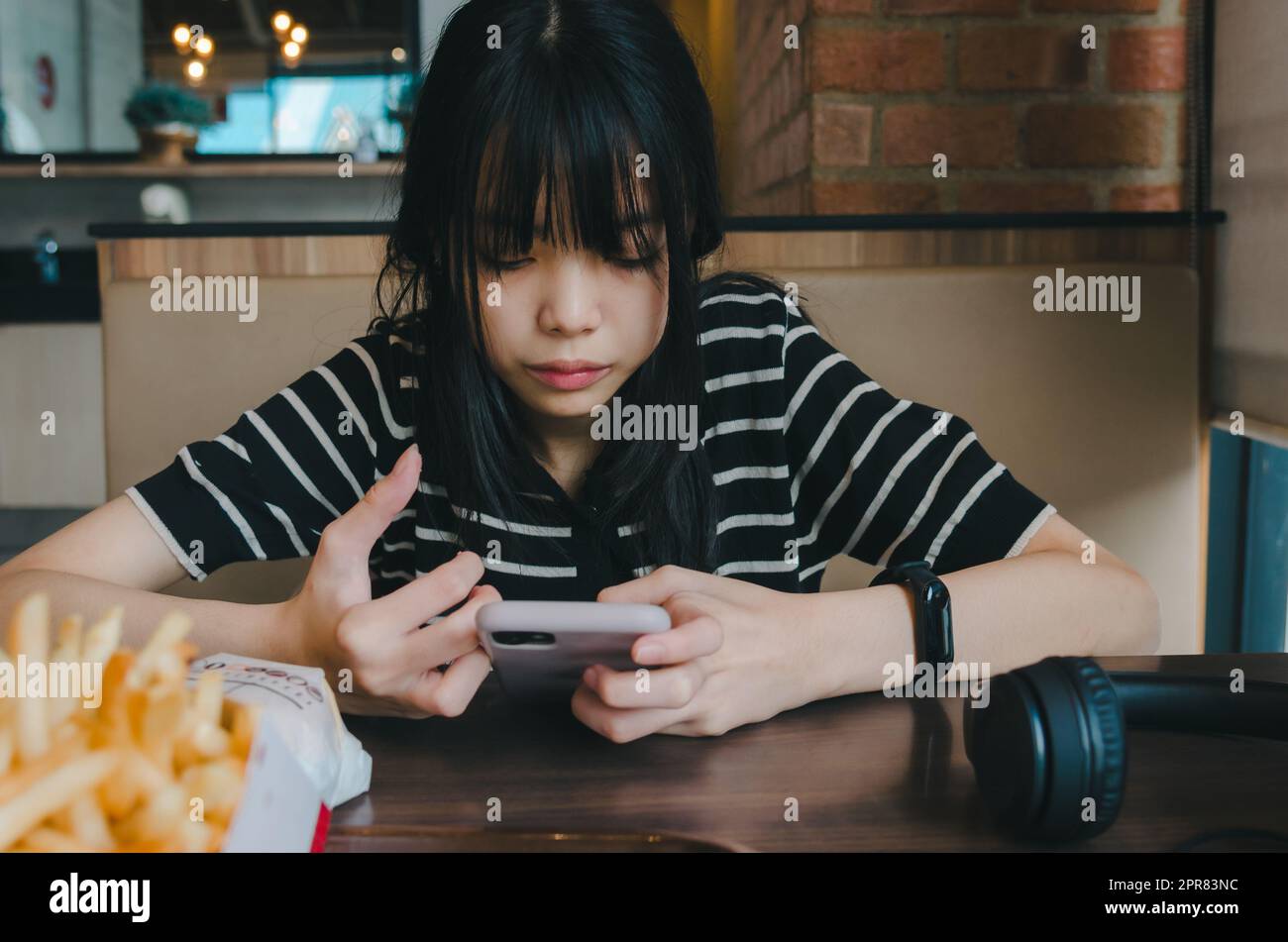 Ragazza adolescente che indossa le cuffie e tiene uno smartphone cellulare social media rilassarsi sul divano. Foto Stock