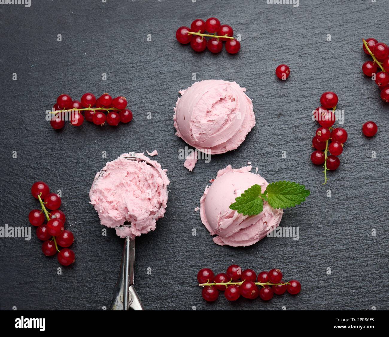 Palline di gelato rosa su un asse di pietra nera, bacche di ribes rosso nelle vicinanze, vista dall'alto Foto Stock