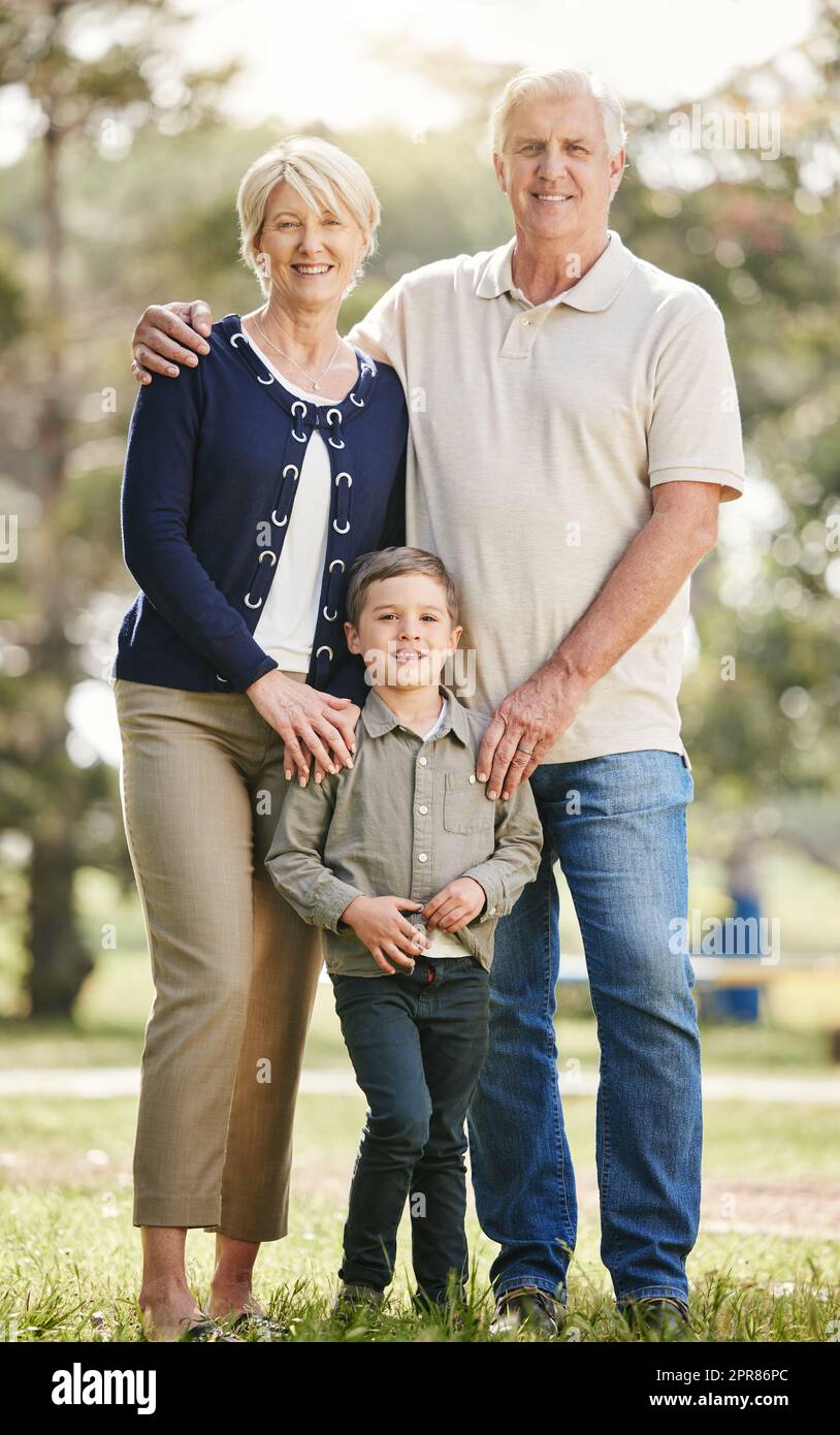 Ritratto di amorevoli nonni caucasici che si divertono con il nipote nella natura. Un bambino sorridente che si unisce a nonna e nonno. Felici anziani e bambini in piedi insieme all'aperto Foto Stock